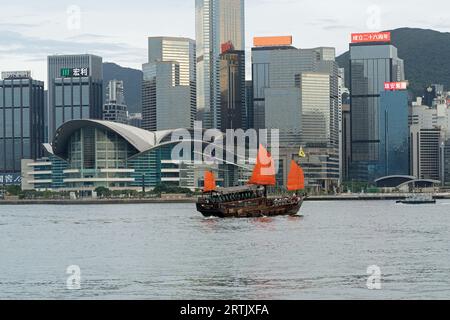 Jonque naviguant sur le port Victoria en journée avec le centre culturel de Hong Kong et la ligne d'horizon derrière. Hong Kong - 25 août 2023 Banque D'Images