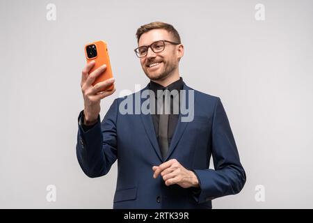 Heureux amical souriant homme d'affaires réussi ayant appel vidéo sur smartphone sur fond gris. Banque D'Images