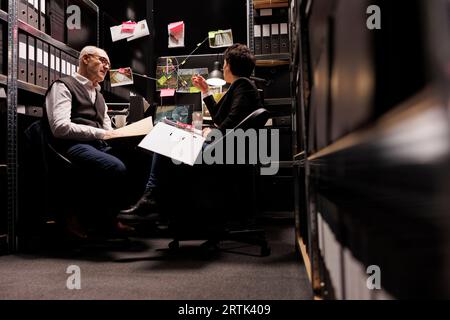 Enquêteurs travaillant des heures supplémentaires aux enquêtes criminelles dans la salle Arhive, analysant le cas de la personne disparue. Détectives privés vérifiant les preuves de la scène de crime, discutant du mystérieux rapport suspect Banque D'Images