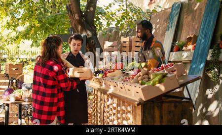 Les clients achètent des aliments bio frais sains sans pesticides, debout au comptoir du marché des agriculteurs. Des vendeurs locaux souriants saluant les clients et vendant des fruits et légumes locaux de la ferme. Banque D'Images