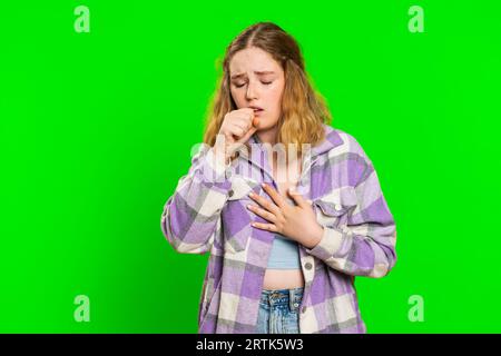 Jeune femme caucasienne en mauvaise santé toussant avec des symptômes de grippe saisonnière couvrant la bouche avec la main, se sentant malade, allergie, fièvre ou infection virale. Fille malade malade isolée sur fond vert de clé chroma Banque D'Images