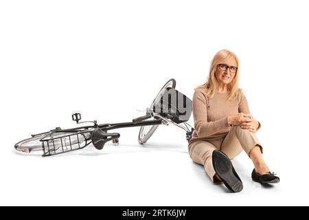 Femme dans la douleur assise sur le sol à côté d'un vélo et tenant son genou isolé sur fond blanc Banque D'Images