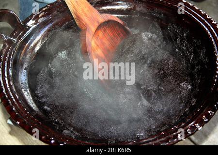 Préparation de taupe rouge, un plat typiquement mexicain dans un pot en argile avec une cuillère en bois géante sur le feu d'un poêle avec tous les ingrédients intégrés Banque D'Images