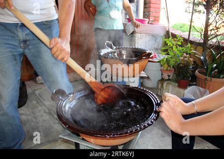 Préparation de taupe rouge, un plat typiquement mexicain dans un pot en argile avec une cuillère en bois géante sur le feu d'un poêle avec tous les ingrédients intégrés Banque D'Images