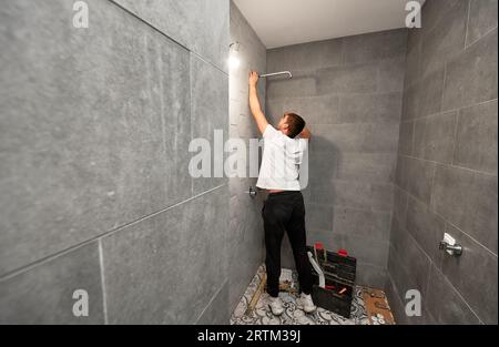 Plombier mâle fixant la pomme de douche de salle de bains tout en travaillant sur la rénovation de salle de bains. Vue arrière du travailleur de l'homme installant la pomme de douche de bain à haute pression à la maison. Banque D'Images