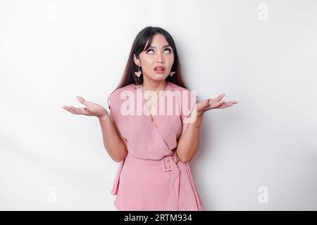 Insatisfait jeune femme asiatique vêtue de chemisier rose roulant ses yeux et levant la main avec mécontentement, debout sur fond blanc Banque D'Images