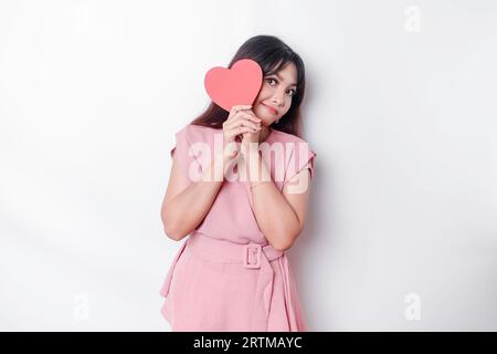 Fille asiatique mignonne et timide rougissant, donnant un papier en forme de cœur rouge, fond blanc isolé Banque D'Images