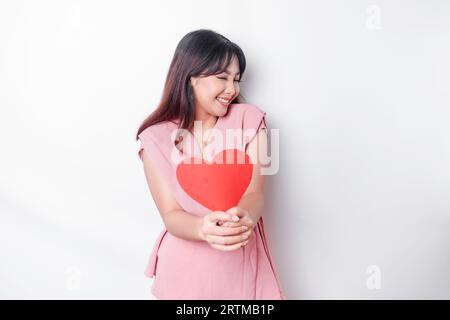 Fille asiatique mignonne et timide rougissant, donnant un papier en forme de cœur rouge, fond blanc isolé Banque D'Images