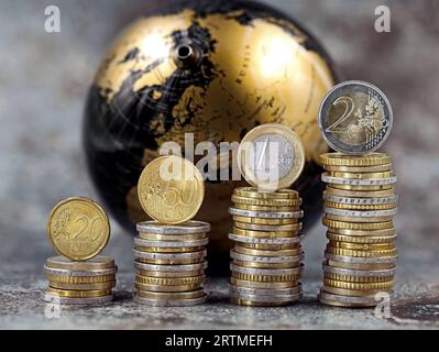 des piles de pièces en euros et en cents symbolisent une augmentation de prix devant un globe noir et or Banque D'Images