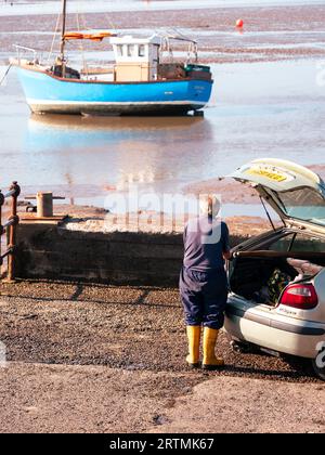 un homme plus âgé dans yellow welly se prépare à monter à bord d'un bateau de pêche près de la muraille du port Banque D'Images