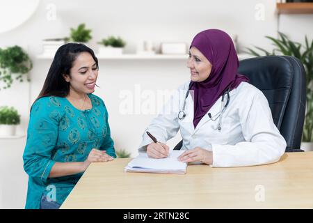 Jeune femme indienne consulte au sujet de son problème avec le médecin musulman féminin portant le hijab dans la clinique moderne. Banque D'Images