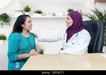 Jeune femme indienne consulte au sujet de son problème avec le médecin gynécologue musulman féminin portant le hijab dans la clinique moderne. Banque D'Images