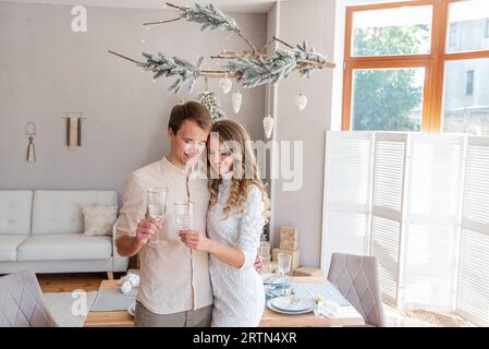 Portrait rapproché d'amour, jeune couple de mode avec des verres de champagne à Noël. Intérieur tendance dans le style scandinave avec fenêtre panoramique Banque D'Images