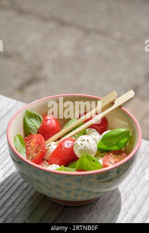 Collation estivale saine avec tomate orange et rouge, basilic, fromage de chèvre et deux brochettes dans un bol. Image verticale avec mise au point sélective et espace de copie. Banque D'Images