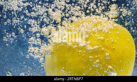 Tranche de citron sous-marine dans de l'eau gazeuse ou de la limonade avec des bulles. Cocktail rafraîchissant soda tonique pétillant. Gros plan de citrons et de glaçons en verre. Lime i. Banque D'Images