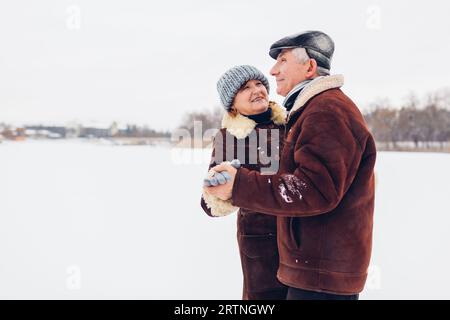 Couple de famille senior dansant à l'extérieur pendant le temps de neige hivernal vêtu de vêtements chauds. Les personnes âgées qui s'amusent à marcher. Espace Banque D'Images