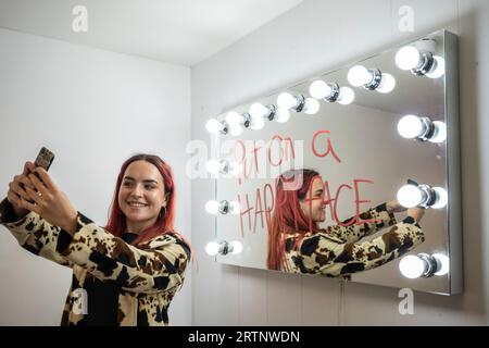 Londres, Royaume-Uni. 14 septembre 2023. Un membre du personnel prenant un selfie à côté du miroir inspiré du Joker lors de l'avant-première de Batman Unmasked au 180 Piccadilly. Marquant la Journée mondiale de Batman, l'histoire légendaire du Caped Crusader est célébrée à travers des bandes dessinées rares, des débuts de Batman à son apparition à la télévision, au cinéma, dans les jeux vidéo et plus encore. Le salon est ouvert au public du 15 au 17 septembre. Crédit : Stephen Chung / Alamy Live News Banque D'Images