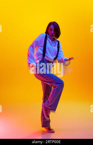Peurs. Image pleine longueur de femme élégante debout avec le visage choqué sur fond de studio orange dans la lumière néon Banque D'Images
