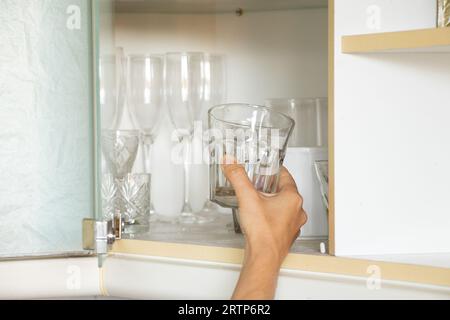 La main d'une femme prend un verre d'une étagère dans un meuble de cuisine dans un appartement, prenant un verre d'une étagère Banque D'Images