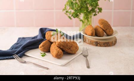 Boulettes de morue, ou « bolinhos de bacalhau » et feuilles de persil sur des plats en céramique blanche dans un comptoir de cuisine. Banque D'Images