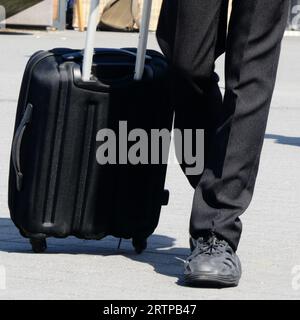 Les jambes d'un homme tirant sa valise trolley Banque D'Images