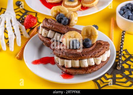 Petit déjeuner drôle pour les enfants pour Halloween. Crêpes sucrées maison créatives sous forme de monstres et symboles traditionnels d'Halloween, avec baies fraîches, chocolat Banque D'Images