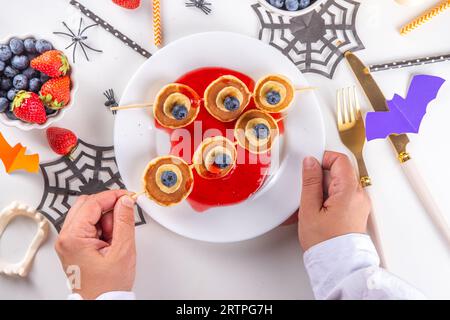 Petit déjeuner drôle pour les enfants pour Halloween. Crêpes sucrées maison créatives sous forme de monstres et symboles traditionnels d'Halloween, avec baies fraîches, chocolat Banque D'Images