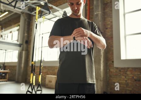 Vérification des résultats. Jeune homme dans des vêtements de sport vérifiant le podomètre tout en se tenant à la salle de gym Banque D'Images