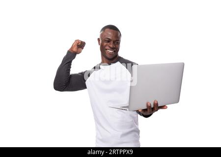 Un jeune homme américain vêtu d'un pull noir et blanc y travaille joyeusement. homme tenant un ordinateur portable Banque D'Images