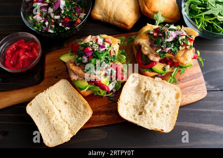 Sandwichs au poulet Chimichurri sur une planche à découper en bois : sandwichs ouverts garnis d'avocat, de poivrons rôtis et de roquette Banque D'Images