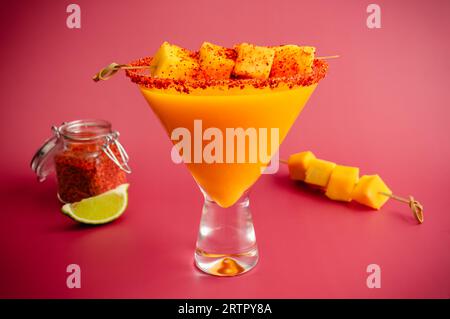 Margarita à la mangue avec une torsade de Chili au curcuma et une garniture de mangue : cocktail de margarita mangue-curcuma avec un bord assaisonné de Chili et de citron vert Banque D'Images