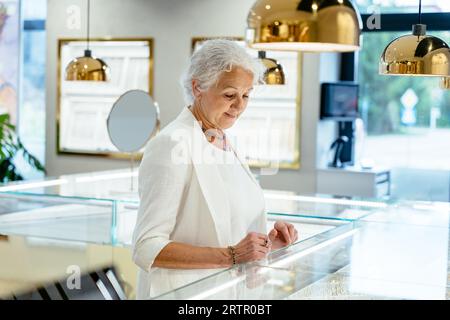 Enior dame consommateur choisissant des bijoux dans le magasin moderne de bijoux d'intérieur.Vente, consumérisme, shopping et concept de personnes. Banque D'Images