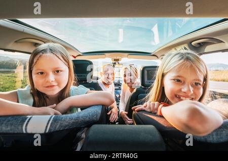 Jeune couple avec filles portrait assis dans une voiture moderne avec un toit transparent. Moments heureux en famille, enfance, restauration rapide ou voyage en auto Banque D'Images