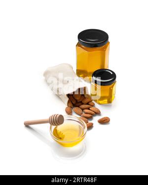 Amandes dans un sac, miel bio dans des bocaux en verre alvéolaire fermés et bol en verre transparent et godet en bois sur fond blanc. Banque D'Images
