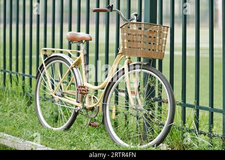 Vélo vintage debout sur l'herbe près de la clôture. Vélo rétro jaune avec panier en osier. Banque D'Images