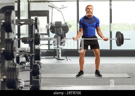 Jeune homme avec barbe et moustache soulevant des poids dans une salle de gym Banque D'Images