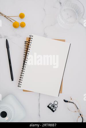 Mise à plat de cahier blanc avec espace de copie pour le texte, les verres et les fleurs jaunes sur fond de marbre blanc. Vue de dessus. Bureau à domicile minimal. Moderne Banque D'Images