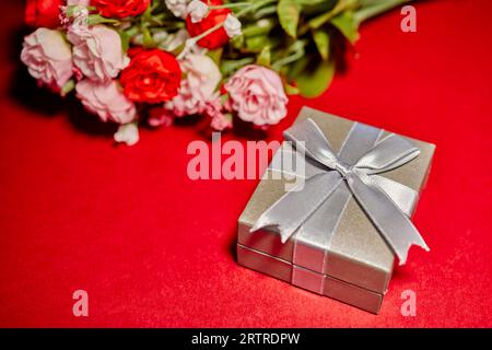 Boîte cadeau argentée avec un noeud et roses en soie isolé sur rouge Banque D'Images