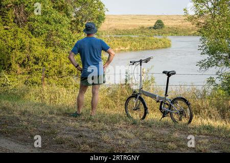 Un homme âgé athlétique regarde Dismal River après avoir monté un vélo pliant dans Whitetail Campground dans la forêt nationale du Nebraska Banque D'Images