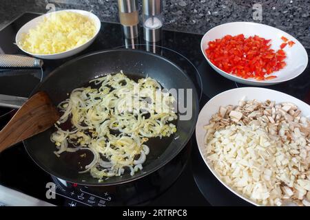 Cuisine souabe, préparation de strudel de pommes de terre copieux, friture des rondelles d'oignon dans la graisse, faire la garniture, racine de persil et champignons coupés sur la droite Banque D'Images