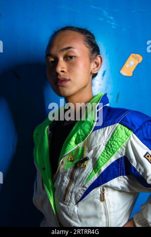 Un homme asiatique gay posant magnifiquement sur un fond bleu la nuit Banque D'Images