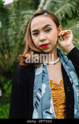 une femme glamour avec un collier de perles et une robe jaune profite d'un jardin plein de fleurs dans l'après-midi Banque D'Images