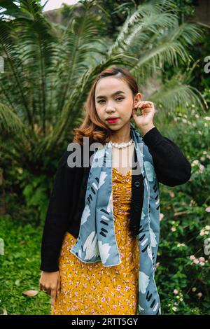 une femme glamour avec un collier de perles et une robe jaune profite d'un jardin plein de fleurs dans l'après-midi Banque D'Images