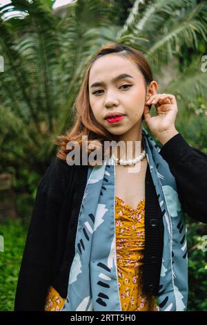 une femme glamour avec un collier de perles et une robe jaune profite d'un jardin plein de fleurs dans l'après-midi Banque D'Images