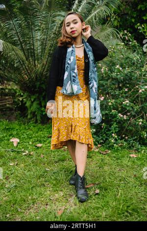 une femme glamour avec un collier de perles et une robe jaune profite d'un jardin plein de fleurs dans l'après-midi Banque D'Images