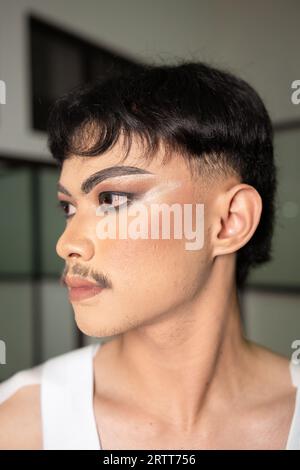 Gros plan sur le visage d'un homme asiatique avec le maquillage lourd et les sourcils foncés vu du côté dans une pièce Banque D'Images