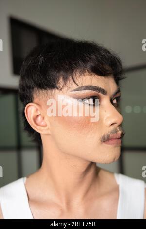 Gros plan sur le visage d'un homme asiatique avec le maquillage lourd et les sourcils foncés vu du côté dans une pièce Banque D'Images