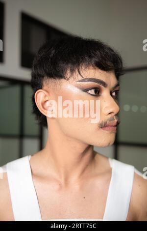 Gros plan sur le visage d'un homme asiatique avec le maquillage lourd et les sourcils foncés vu du côté dans une pièce Banque D'Images