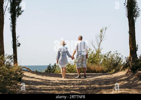 Heureux couple de personnes âgées se tiennent la main, se tiennent parmi les arbres, regardent la mer. Profitez de la vue sur la mer. Banque D'Images