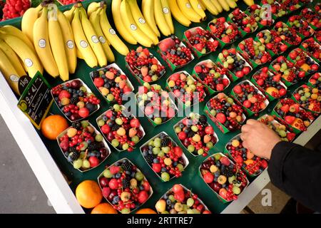 Vendeur de fruits arrangeant un punnet de papier de baies sauvages. Rangées de fruits frais exposées dans un petit magasin local de la rue Desaix, Paris, France. Banque D'Images